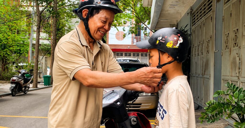 Ông Ngô Chí Ngọ cài mũ bảo hiểm cho cháu nội trước giờ đến trường, hình ảnh đời thường phản ánh nhịp sống năng động của người đàn ông 72 tuổi.