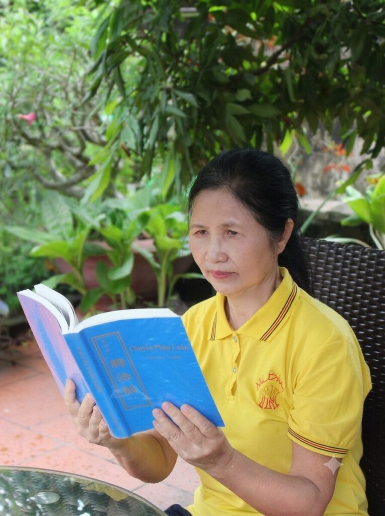 Cô giáo Bùi Thị Hà đọc sách giữa không gian sân vườn tại nhà, ghi lại khoảnh khắc đời thường của nhân vật trong bài cô giáo vượt qua bệnh tật hiểm nghèo.
